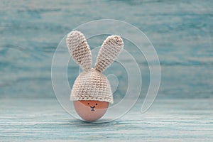 Easter egg in crochet hat with bunny ears against painted shabby wooden background