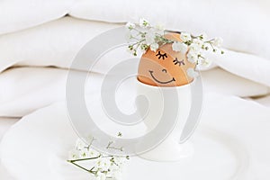 Easter egg with cute face in floral wreath crowns in egg cup on white background