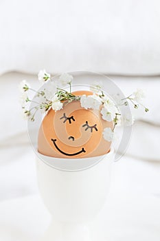 Easter egg with cute face in floral wreath crowns in egg cup on white background