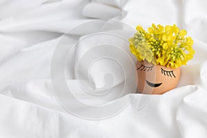 Easter egg with cute face and wreath of yellow flowers on white fabric background