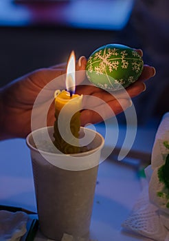 Easter egg in the master's hands above candle flame