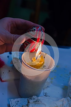 Easter egg in the master's hands above candle flame