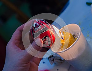 Easter egg in the master's hands above candle flame