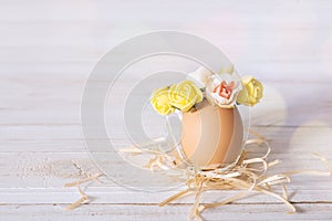 Easter egg on a white desk. Funny easter egg decorated yellow roses wreath