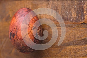 Easter egg on wooden background. Painted brown with spots and cracks. Closeup macro shot with copyspace