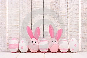 Easter eggs against white wood, two with bunny faces and ears