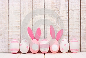 Easter eggs against white wood, two with bunny tails and ears