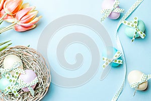 Easter eggs background. Colorful egg with tape ribbon, spring tulips, feathers on pastel blue background in Happy Easter