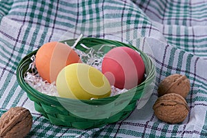 View of a wicker basket with colorful Easter eggs on a white green tablecloth or napkin. Decorative background with space for