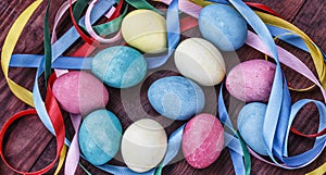 Easter eggs in basket with colorful ribbons, spring flowers selective focus. Top view, horizontal.