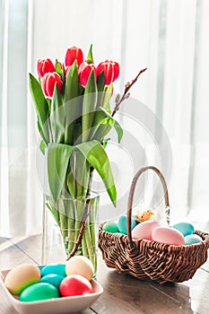 Easter eggs in a basket with red tulips in a vase
