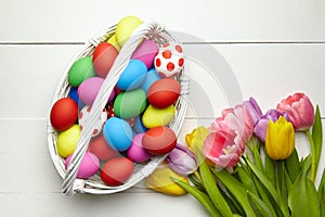 Easter eggs in basket and spring colorful flowers on white wooden table top view