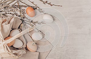 Easter eggs in basket and willow branches on a grey wooden background, rustic style. Banner photo