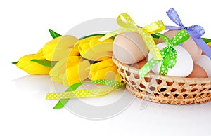 Easter eggs in the basket and yellow tulips isolated on a white