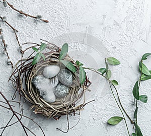 Easter eggs in bird nest with feather and spring flowers on white background. Happy Easter holiday, top view, flat lay.