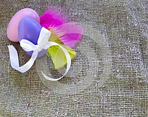 Easter eggs with bow knot and colored feathers  on burlap background