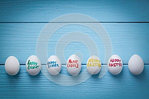 Easter eggs with color titles `Happy Easter` written by brush are on the blue colored wooden background with vignette effect