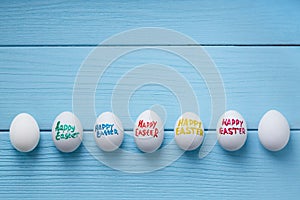 Easter eggs with color titles `Happy Easter` written by paint brush are on the blue colored wooden background.
