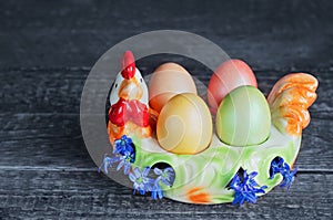Easter eggs on a colorful chicken-shaped plate, on a wooden background