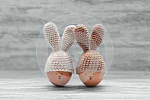 Easter eggs in crochet hats with bunny ears against painted shabby wooden background