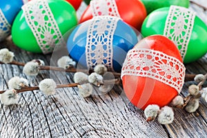 Easter eggs decorated with lace and willow branch on wooden background