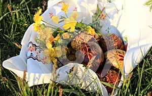 Easter Eggs Decorated with Natural plants and Flower blossoms and Boiled in Onions Peels in woven basket in green grass.