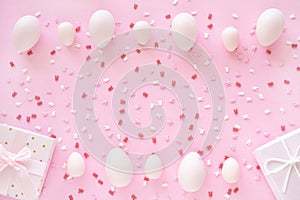 Easter eggs frame with bunny ears sugar sprinkle and gift box on pink background.
