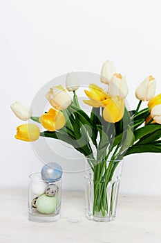 Easter eggs in a glass and yellow tulips in a vase on a light background