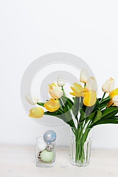 Easter eggs in a glass and yellow tulips in a vase on a light background