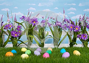 Easter eggs on grass, flowers on fence, sky background