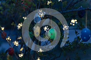 Easter eggs hang from a tree and are illuminated indirectly with a string of lights