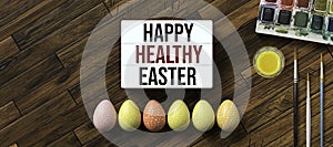 Easter eggs with message HAPPY HEALTHY EASTER surrounded by brushes and water color boxes