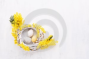 Easter eggs and mimosa wreath on a white background. Top view, copy space