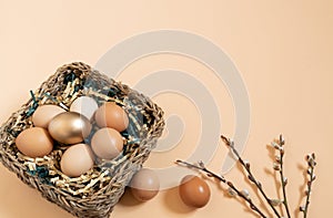 Easter eggs natural and gold in basket with paper filler . Branch of willow catkinsan. Light pastel orange background