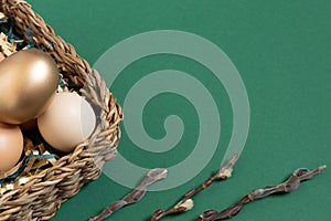 Easter eggs natural and gold in basket with paper filler . Branch of willow catkinsan. Light pastel orange background
