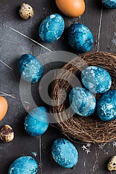 Easter eggs in nest painted by hand in blue color on dark background