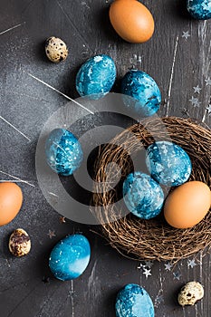 Easter eggs in nest painted by hand in blue color on dark background