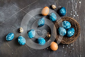 Easter eggs in nest painted by hand in blue color on dark background