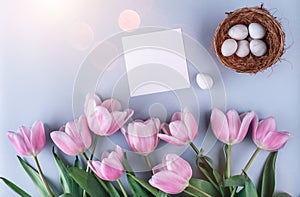 Easter eggs in nest and tulips flowers on blue background with card. Happy Easter. Top view with copy space