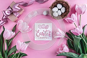 Easter eggs in nest and tulips flowers on pink background with Easter card.