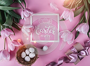 Easter eggs in nest and tulips flowers on pink background with Easter card. Waiting for spring. Top view with copy space