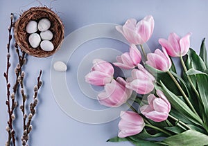 Easter eggs in nest and tulips flowers on spring background.