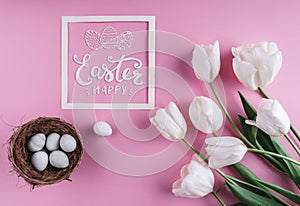 Easter eggs in nest and white tulips flowers on pink background with Easter card.