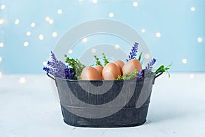 Easter eggs in an old bowl, grass, flowers on a blue background with bokeh. Easter and spring concept