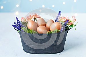 Easter eggs in an old bowl, grass, flowers on a blue background with bokeh. Easter and spring concept