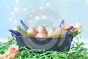 Easter eggs in an old bowl, grass, flowers on a blue background with bokeh. Easter and spring concept