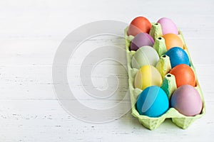 Easter eggs painted brightness colors in green carton tray on wooden background