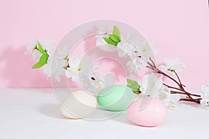 Easter eggs, pink, beige and green, on a concrete white table, next to flowers on a pink background. Pastel shades. Copy space