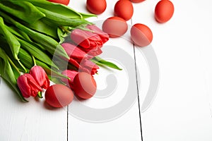 Easter Eggs and red flowers on white wooden table. Painted chicken eggs and red tulip