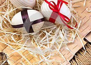 Easter eggs with ribbon and red flowers. Background birch bark and straw